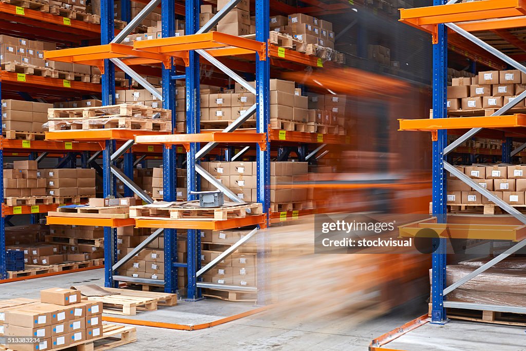 Forklifts carrying cardboard box in warehouse.