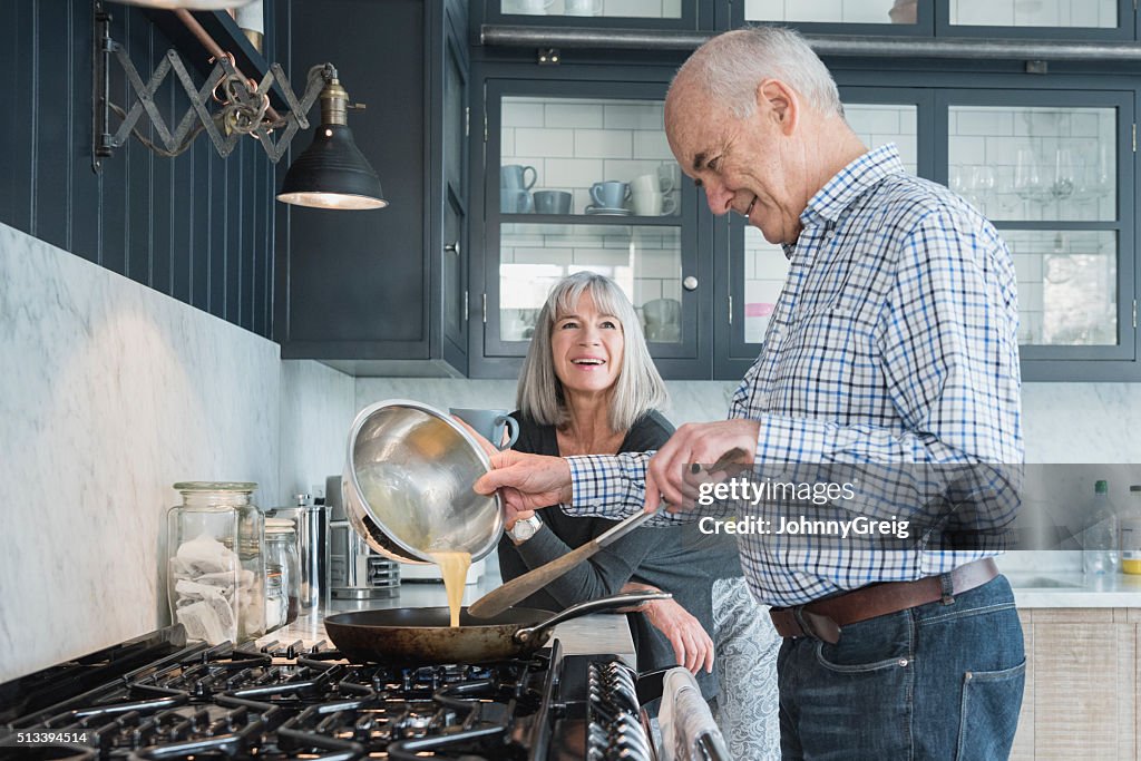 Senior man holding bowl making dinner, his wife is watching