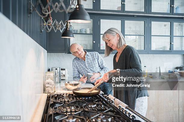 senior woman cooking dinner talking to her husband - hob 個照片及圖片檔