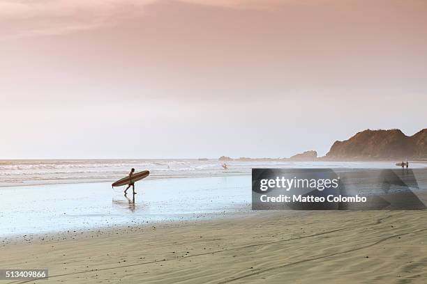 surfer walking on the beach at sunset, costa rica - nosara costa rica stock pictures, royalty-free photos & images