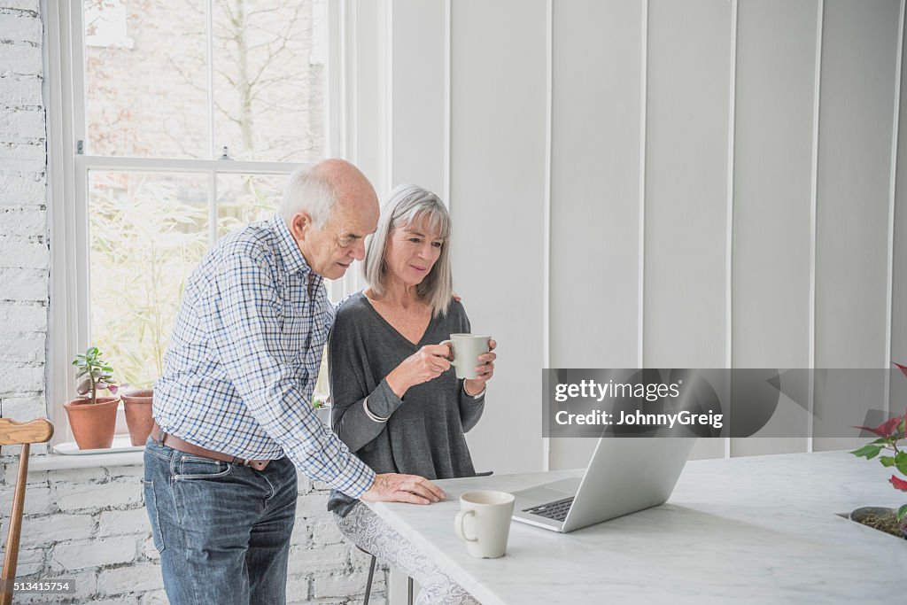 Senior couple using laptop, woman holding coffee