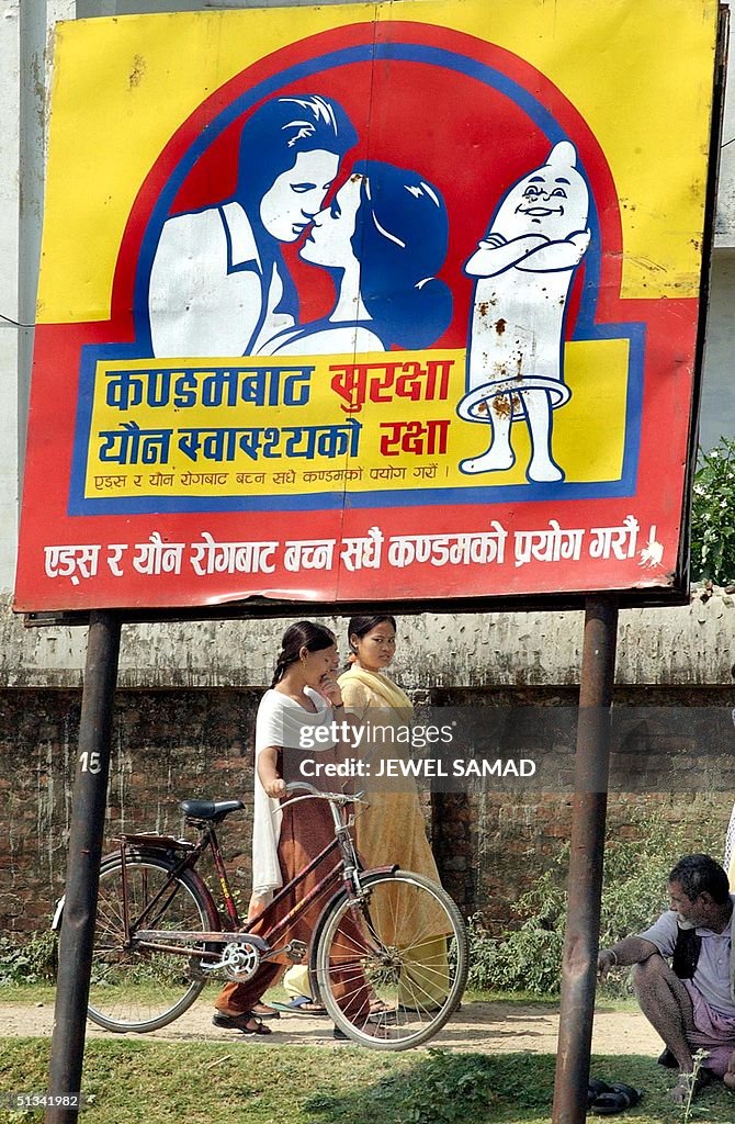 Two Nepalese women walk past a billboard urging pe