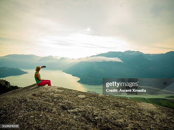 woman takes smart phone pic on mtn summit - woman smartphone nature stockfoto's en -beelden