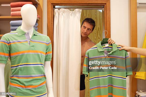 man trying on tshirt in shop dressing room - mens changing room stock pictures, royalty-free photos & images