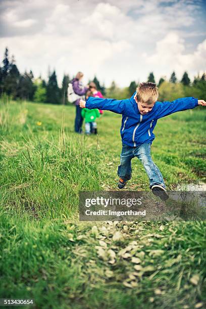 piccolo ragazzo salto nel fango da hiking - family hiking in spring outdoors foto e immagini stock