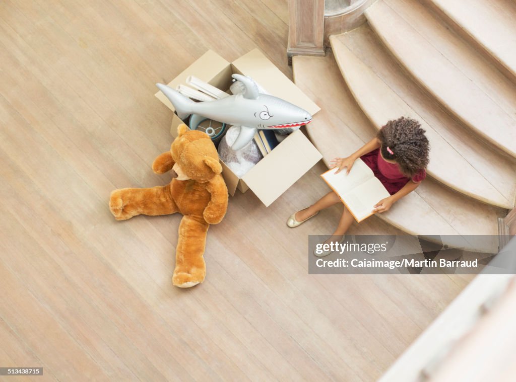 Young girl reading on stairs with toys