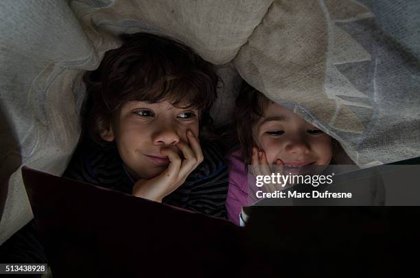 little boy and girl reading under bed sheets before sleep - kids sleep in bed stockfoto's en -beelden