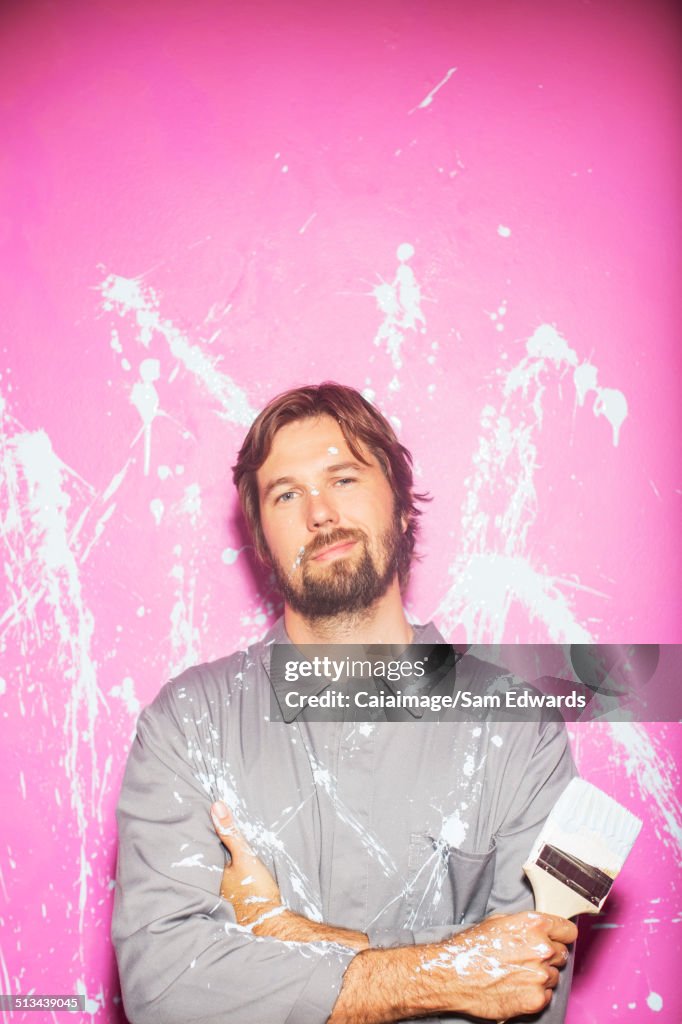 Man smiling in front of wall holding paintbrush