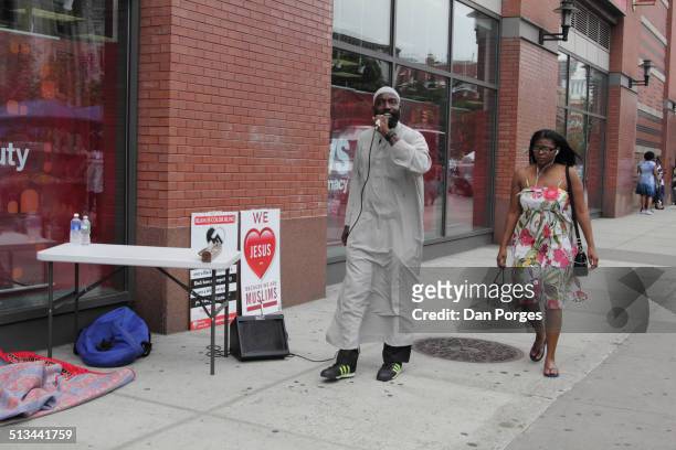 Man uses a portable microphone and amplifier to preach near the intersection of 125th Street and Malcolm X Ave in Harlem, New York, New York, August...