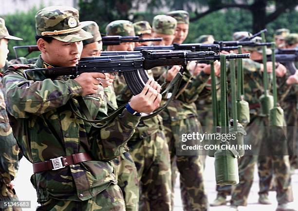 Chinese People's Liberation Army soldiers train to hold their rifles steady by hanging water bottles on the barrels during a workout near their...