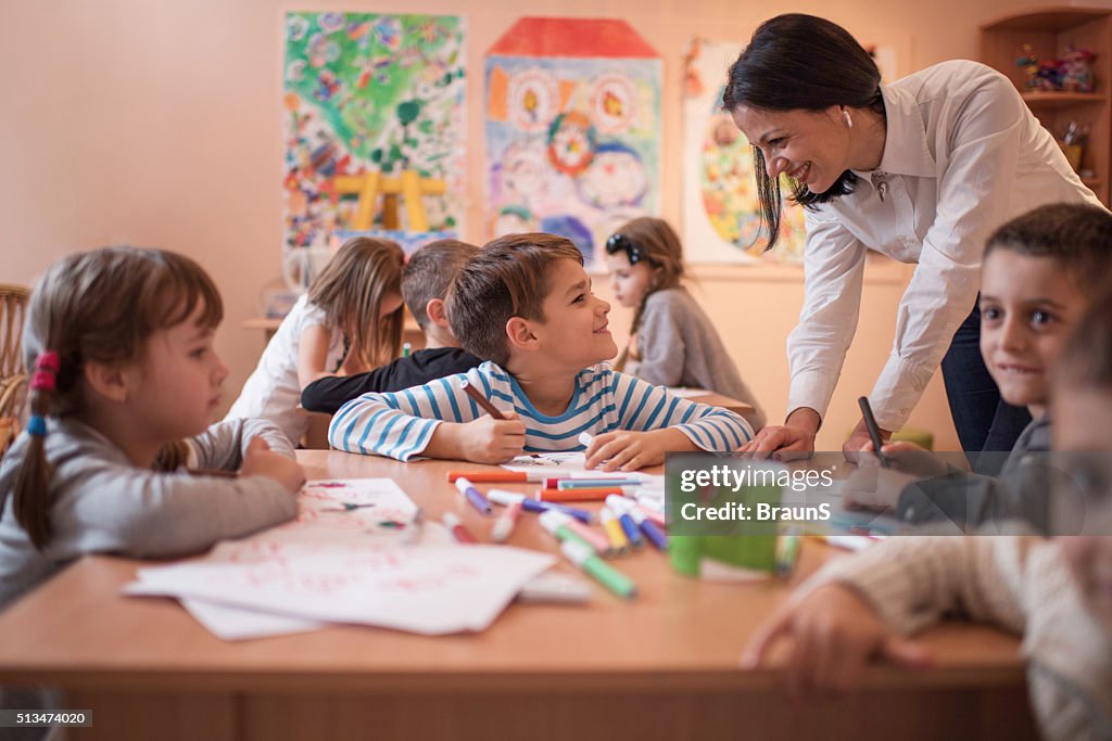 Smiling boy talking to his preschool teacher during art class.