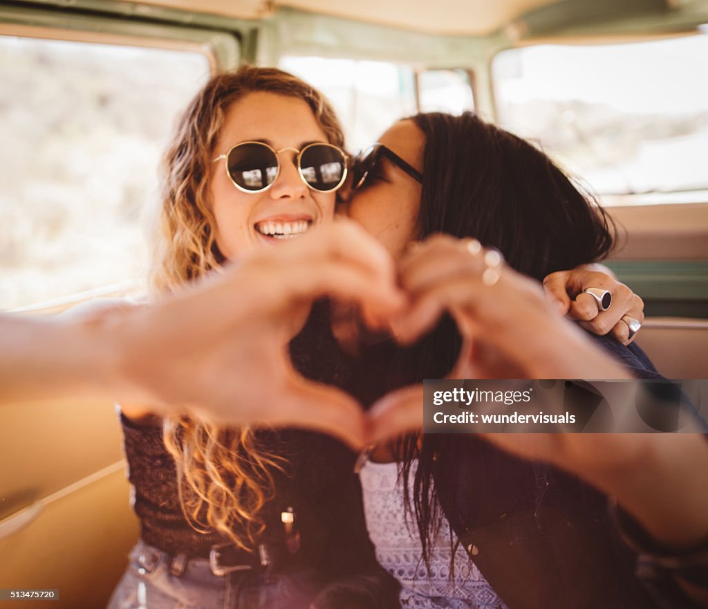 Woman kissing her girl friend on cheek with hand heart