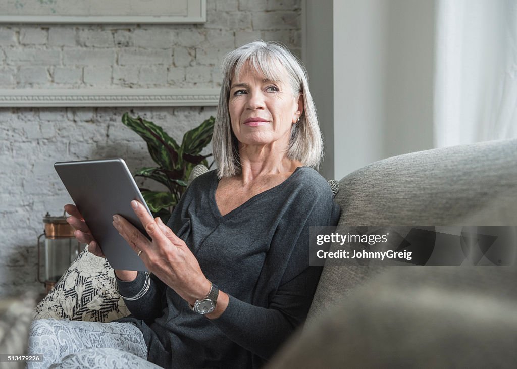 Senior woman looking away, holding digital tablet