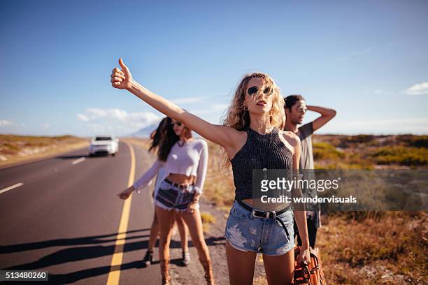 hipster multi-ethnic group of friends hitchhiking on highway - hitchhiking 個照片及圖片檔