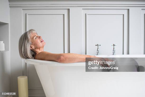 senior woman relaxing in bath with eyes closed - beautiful woman bath stockfoto's en -beelden