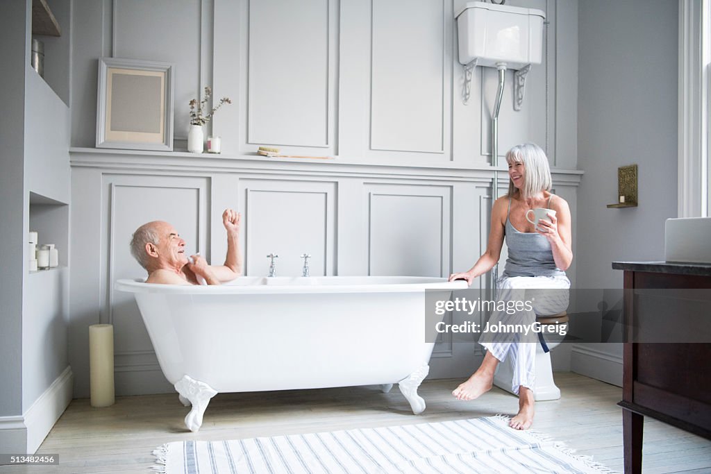 Senior man in bath talking to wife in hotel bathroom