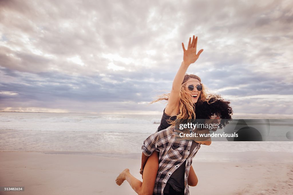 Boho-Mädchen Reiten Huckepack nehmen auf hipster Mann am Strand