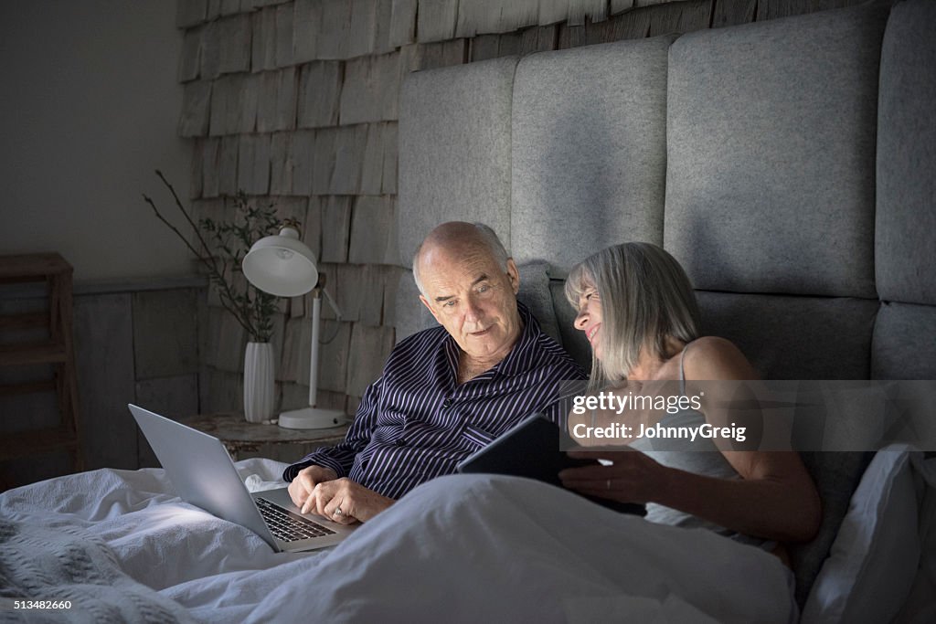 Senior couple in bed using laptop and digital tablet