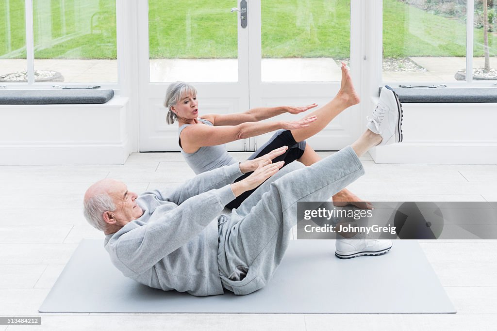 Senior man copying female fitenss instructor stretching legs