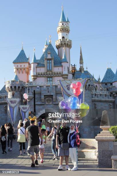 View of an unidentified couple as they pose with Mickey Mouse balloons in front of the Sleeping Beauty Castle at the Disneyland amusement park,...