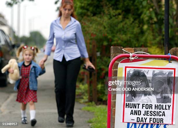 Woman and her child passes a poster with pictures of Holly Wells and Jessica Chapman in the village of Soham's high street 08 August 2002. The search...