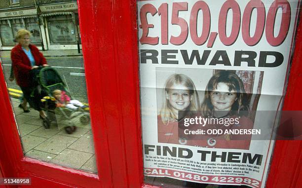 Woman and her child is reflected in the window carrying a poster with pictures of Holly Wells and Jessica Chapman in the village of Soham's high...