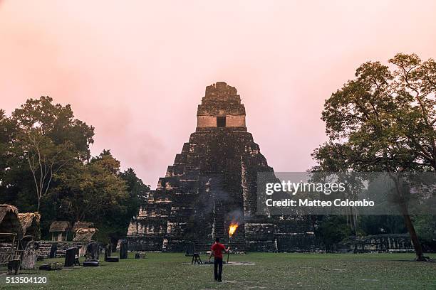 local man holding a torch in front of mayan temple, tikal, guatemala - mayan people stockfoto's en -beelden