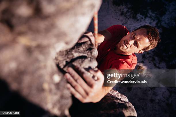 focussed rock climber holding on grip while hanging from boulder - zekeren stockfoto's en -beelden