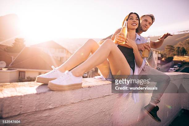 jeune hipster couple appréciant une bière sur le toit au coucher de soleil - éclat rire femme photos et images de collection