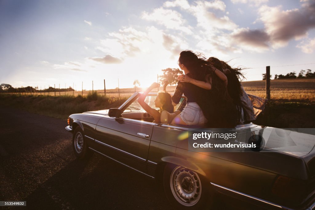 Teenager friends embracing joyfully on their road trip at sunset