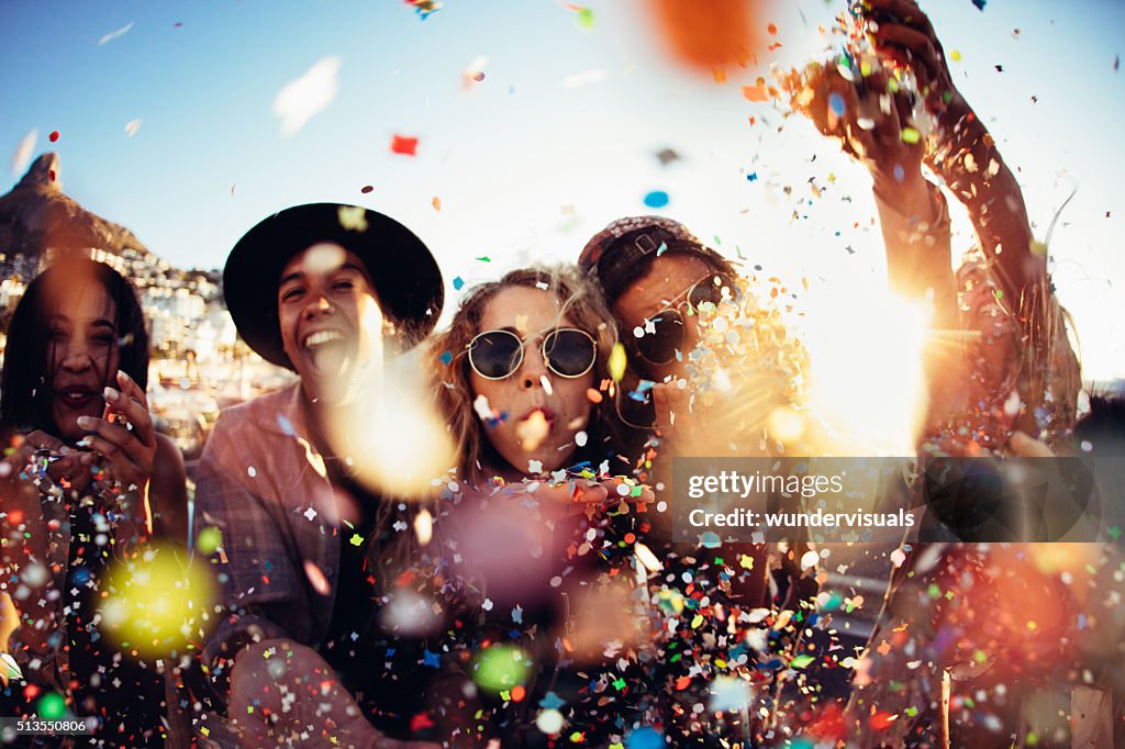 Teenager hipster friends partying by blowing colorful confetti from hands