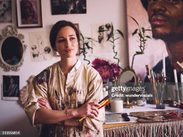 artist in her studio wearing paint covered smock with paintbrush - fine art woman stockfoto's en -beelden