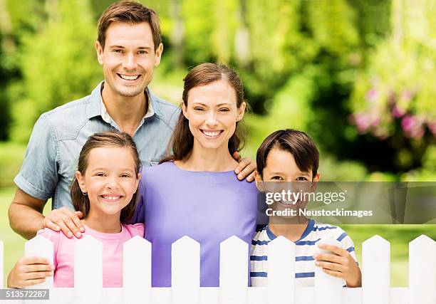 famiglia felice in piedi dietro steccato in giardino - steccato foto e immagini stock