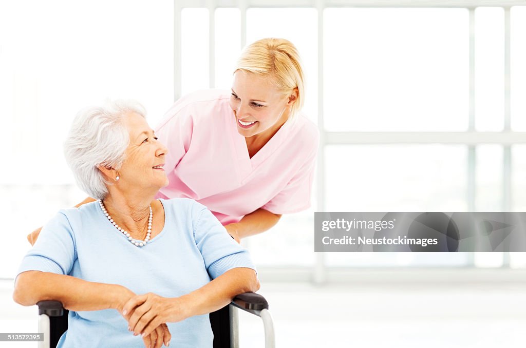 Nurse Looking At Senior Woman While Pushing Wheelchair