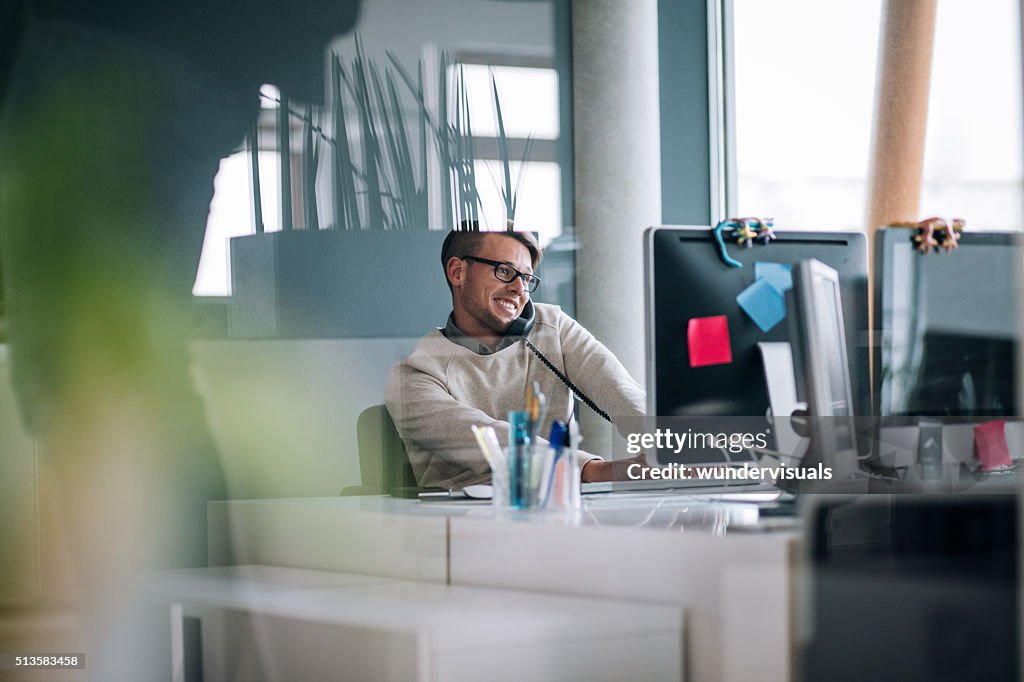 Young business man typing on computer while on phone