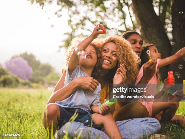 giovane famiglia afro-americana attraente che soffia bolle nel - blowing bubbles foto e immagini stock
