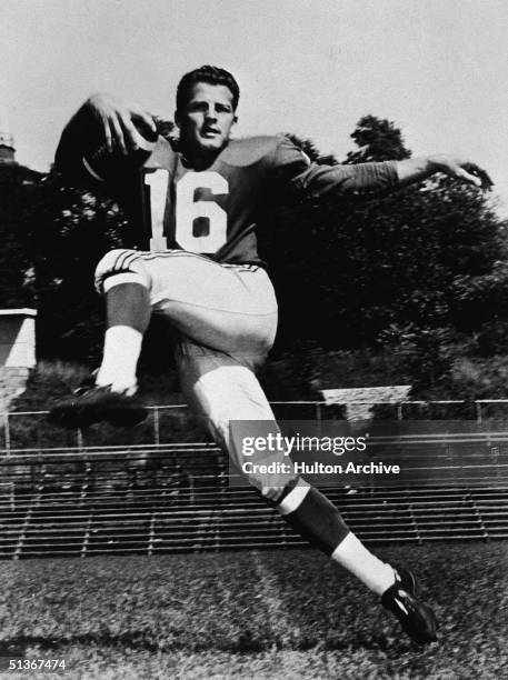 American football runningback Frank Gifford of the New York Giants leaps gracefully through the air with a football in one hand and the other arm...