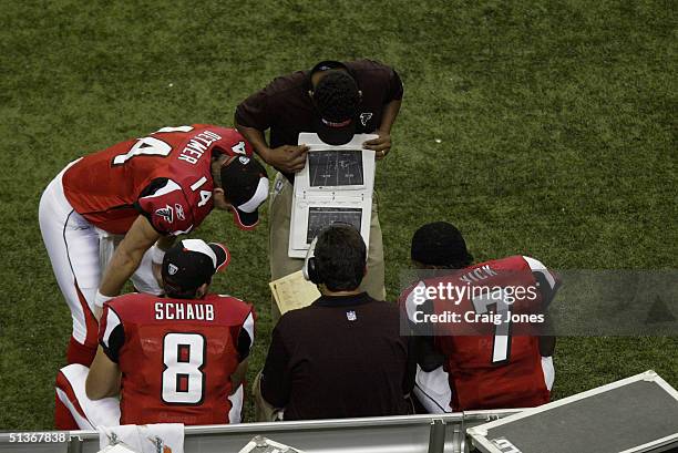 Quarterback Michael Vick of the Atlanta Falcons examines a playbook with his teammates, quarterback Matt Schaub, quarterback Ty Detmer, and head...