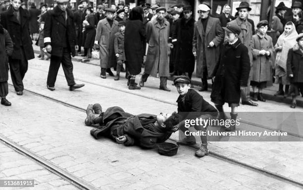 Photograph of a young boy helping a man who collapsed along the tram tracks in the Warsaw Ghetto. Dated 1941