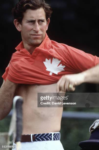 Prince Charles pulls on the Polo shirt of his team the 'Maple Leafs' before a Polo match on August 2, 1982 at Cowdray Park, West Sussex.