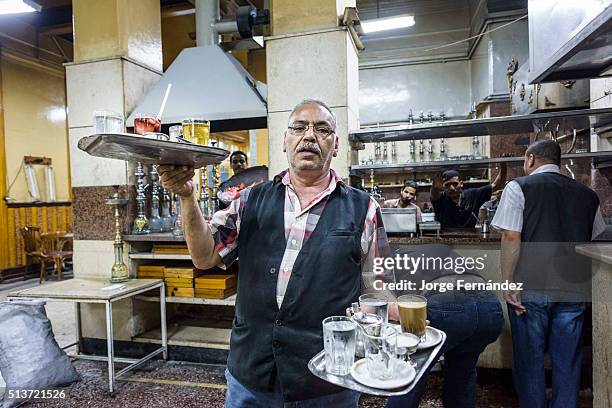Waiter in a busy coffe shop carrying two trays ful os drinks.