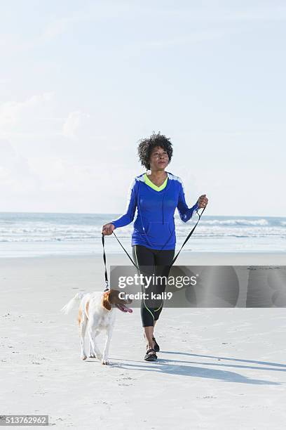 mature black woman walking dog on beach - mature adult walking dog stock pictures, royalty-free photos & images