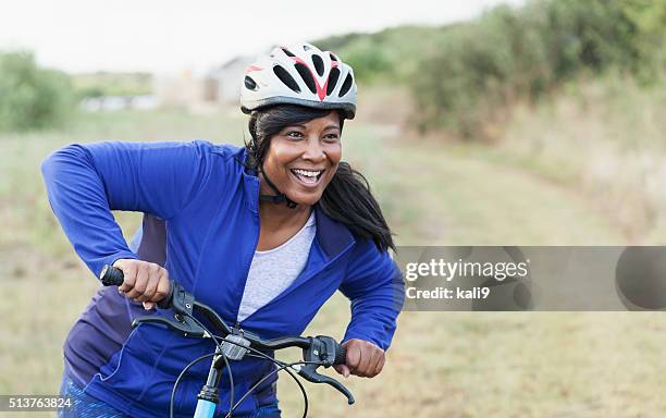 african american woman riding bike in park - adult riding bike through park stock pictures, royalty-free photos & images