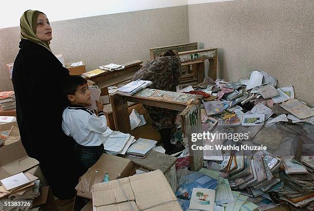 Muhammad Abdulrazaq, age 6, stands with his mother to receive text books as a teacher searches for decent copies from a pile of old school books at...