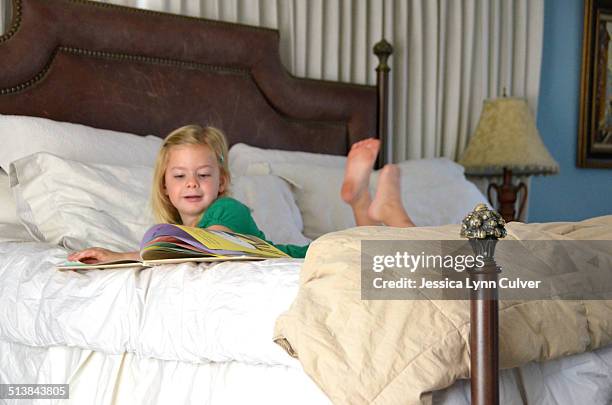 little girl lying on a bed looking at books - barefoot feet up lying down girl stockfoto's en -beelden