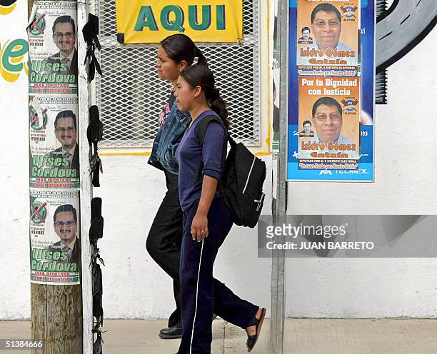 Mujeres pasan junto a carteles de candidatos municipales en San Cristobal, al sureste de Ciudad de Mexico el 02 de octubre de 2004. El estado...