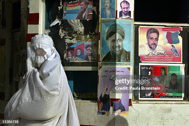 An Afghan woman walks past election posters as election officials prepare for the presidential elections October 3, 2004 in Mazar I Sharif,...