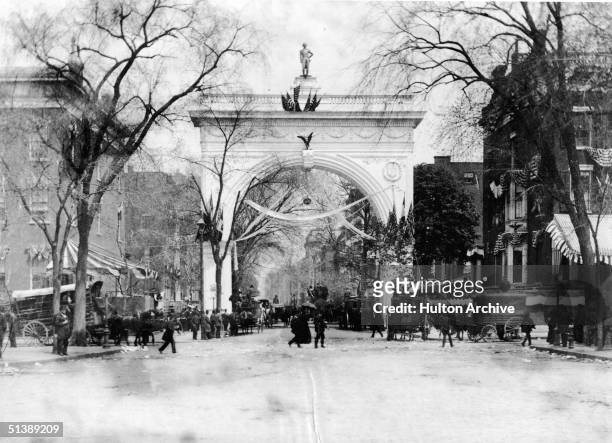 People walk and ride carriages near the arch, covered in papier-mache wreaths, garlands of flowers, and American flags, in Washington Square Park...