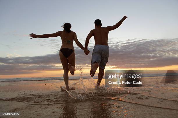 couple runng into sea at sunset - couple sea uk stock pictures, royalty-free photos & images