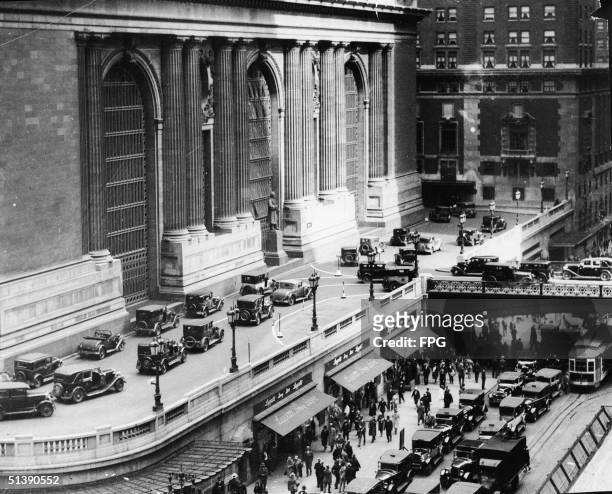 Large group of pedestrians walks on the sidewalk below as cars drive above on the bifurcated and elevated section of Park Avenue which goes around...
